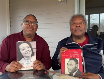 Gregory Foster holding Coretta Scott King's memoir 'My Life, My Love, My Legacy' and Rev. Joel King holding a Martin Luther King Jr. biography, seated together on a porch.