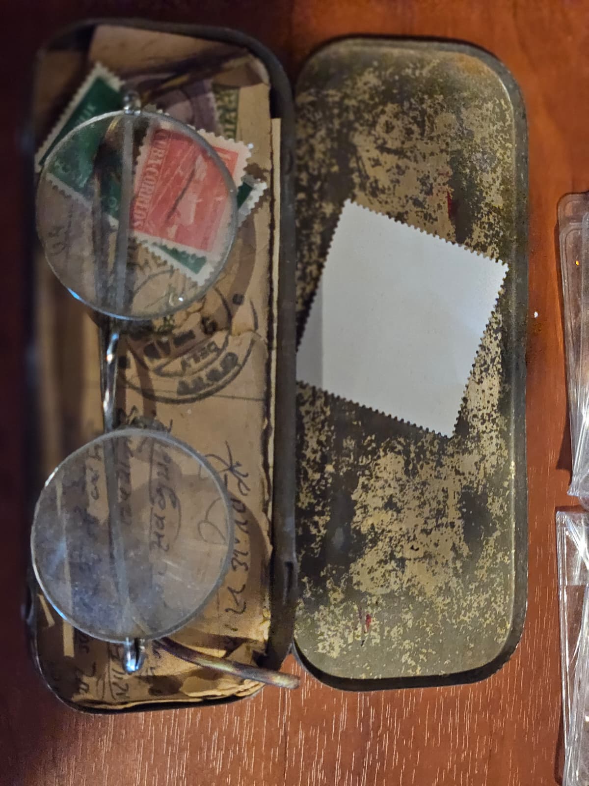 A pair of replica Gandhi-style round eyeglasses in a vintage metal case lined with period postage stamps and handwritten notes